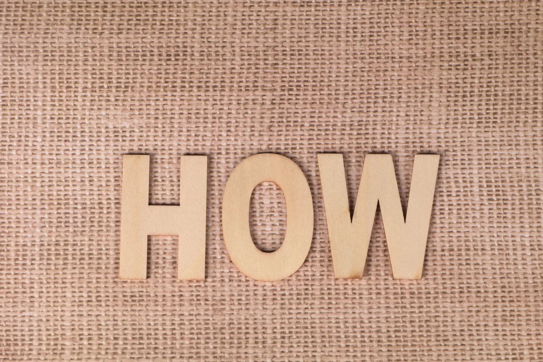 Word 'HOW' formed with wooden letters on textured burlap surface.